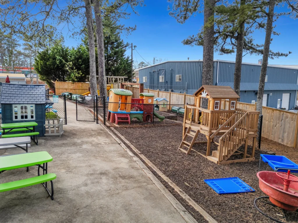 Playground area at Chroma Early Learning Academy featuring a wooden play structure, colorful play equipment, green picnic tables, and a fenced environment, emphasizing a nurturing space for children's growth and development in Duluth, GA.