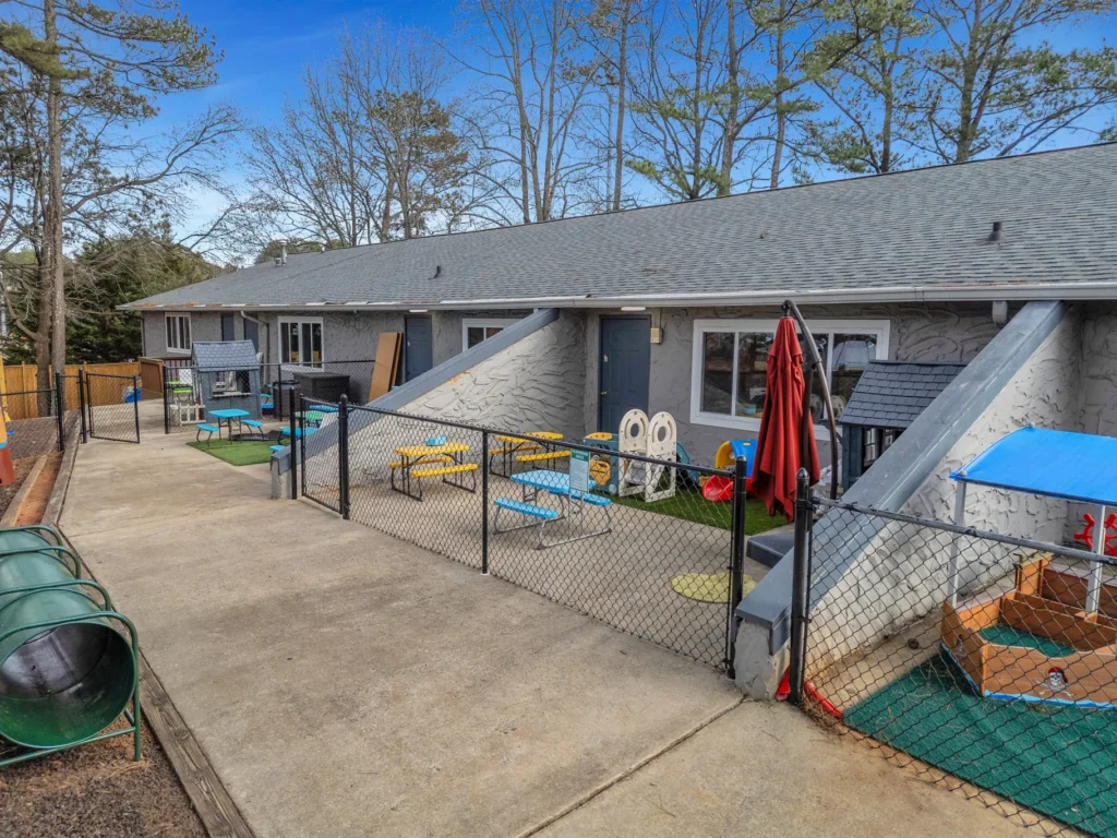 Playground area of Chroma Early Learning Academy's Pleasant Hill Campus, featuring colorful outdoor furniture, play structures, and safety fencing in a nurturing environment for children's growth and development.