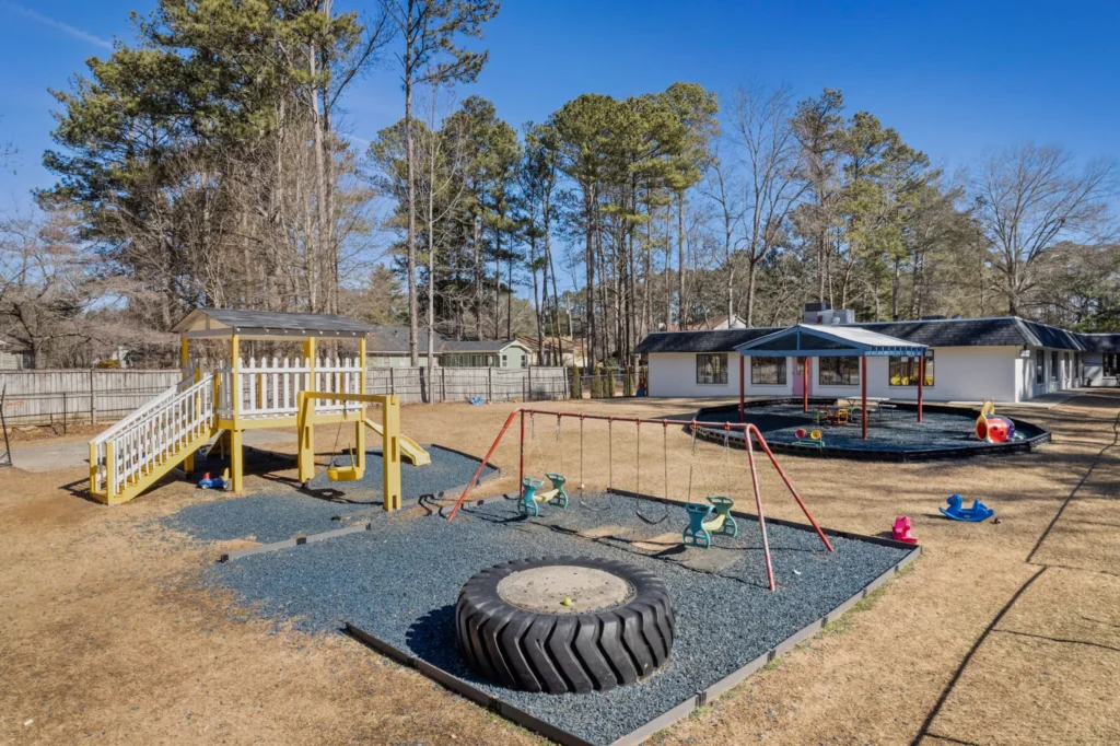 Playground at Chroma Early Learning Academy featuring a yellow play structure, swings, and a tire, surrounded by a safe, engaging outdoor environment for children in Marietta, GA.
