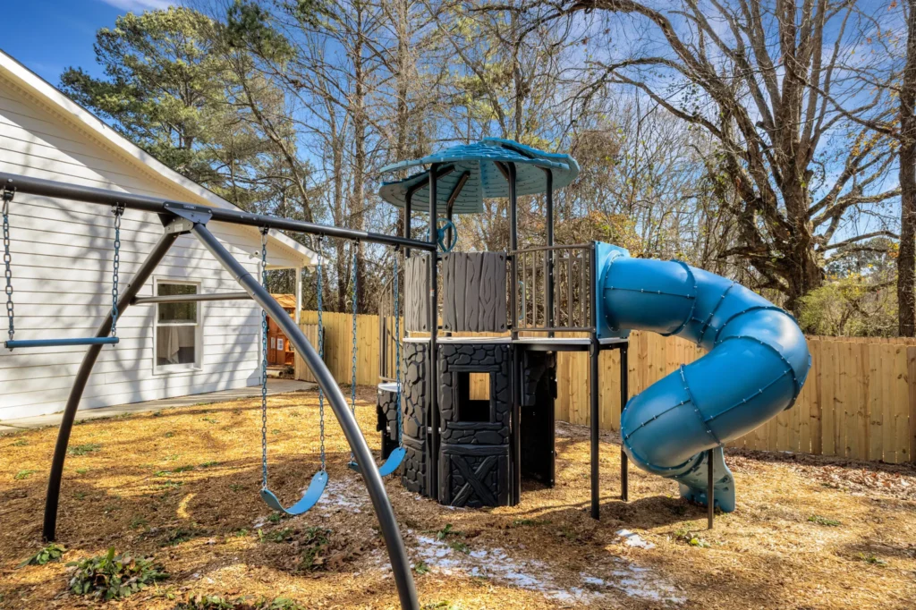 Playground equipment featuring a blue slide and swings in a secure outdoor area at Chroma Early Learning Academy, Ellenwood Campus, designed for children's exploration and play.