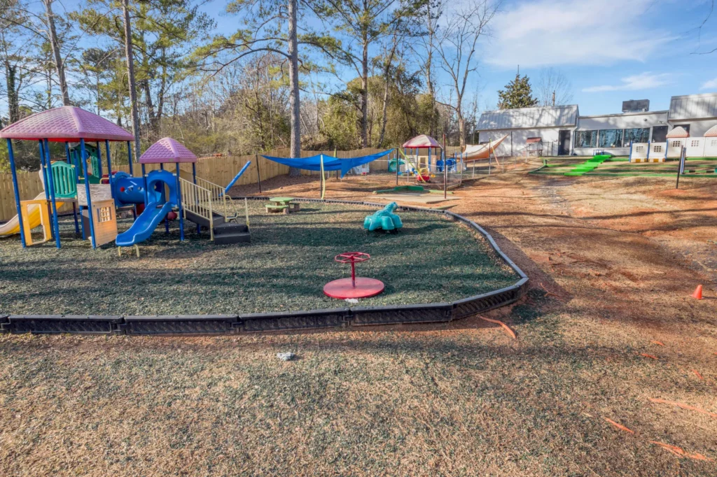Playground area at Chroma Early Learning Academy in Lilburn, featuring colorful play structures, a slide, a merry-go-round, and shaded seating, set in a safe outdoor environment designed for children's exploration and play.