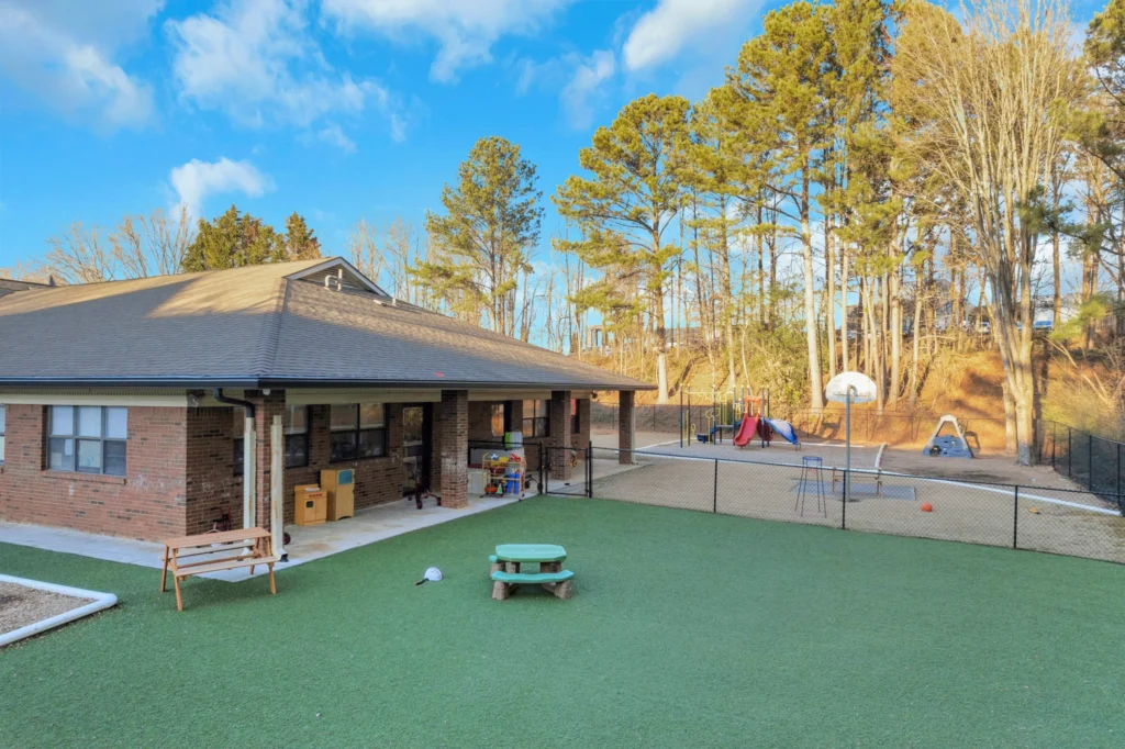 Chroma Early Learning Academy Satellite Blvd Campus outdoor play area with playground equipment, grassy surface, and surrounding trees, emphasizing a safe and nurturing environment for children's development.
