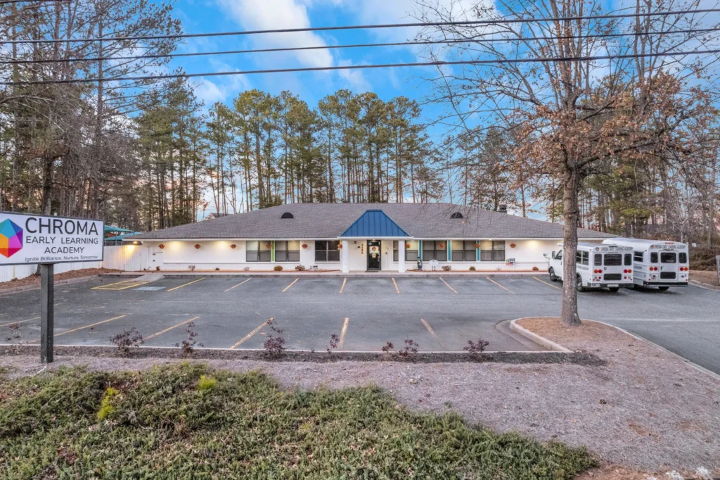 Chroma Early Learning Academy building exterior with sign, showcasing preschool and childcare services in Johns Creek, GA, surrounded by trees and parking area.