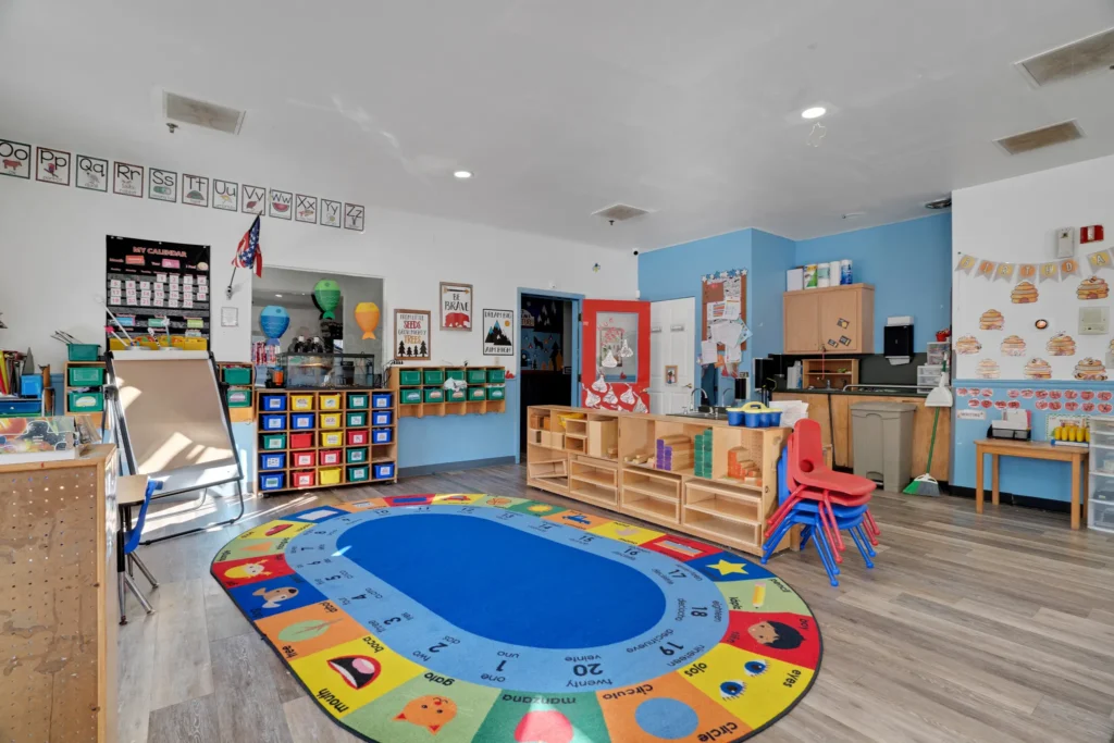 Bright and colorful classroom at Cherokee Academy featuring a circular rug with educational graphics, colorful storage bins, and a welcoming environment for early childhood education.