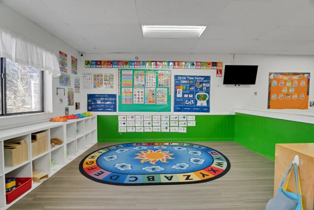 Classroom interior at Chroma Early Learning Academy's Tyrone Campus featuring colorful educational posters, a circular rug with letters, and organized storage for toys and learning materials.