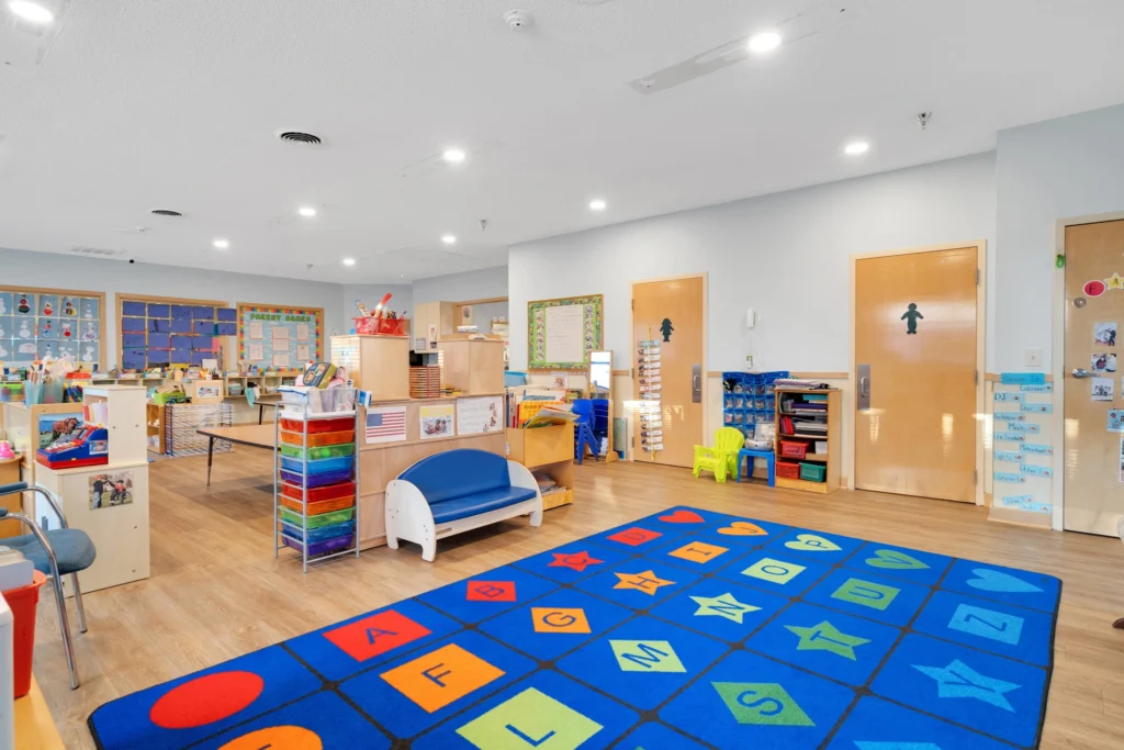Bright and inviting classroom at Chroma Early Learning Academy, featuring colorful educational rugs, activity tables, storage units with art supplies, and engaging learning materials, emphasizing a nurturing environment for children's development.