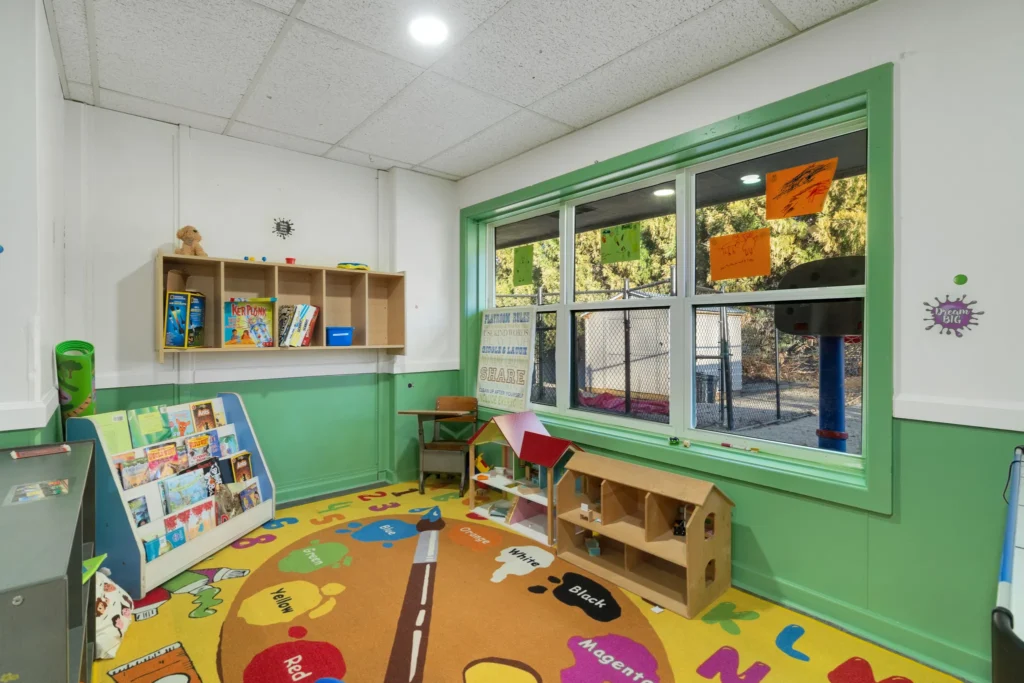 Brightly colored early learning classroom at Chroma Early Learning Academy, featuring bookshelves, educational toys, and a vibrant carpet with letters and numbers, designed for children aged 6 weeks to 12 years.