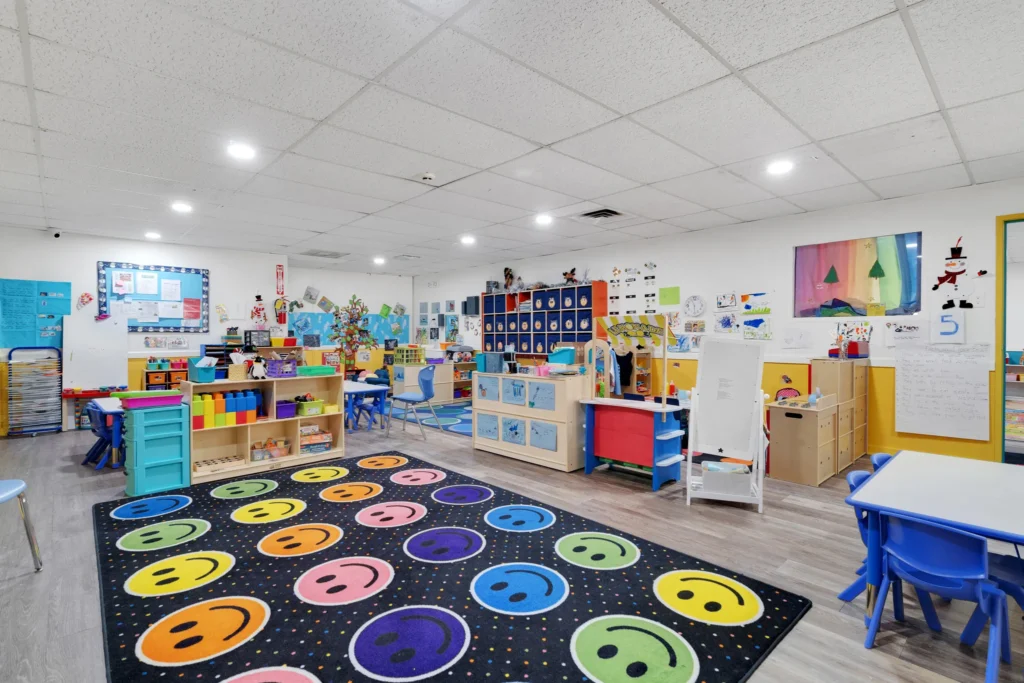 Bright and colorful early learning classroom at Chroma Early Learning Academy, featuring cheerful smiley face carpet, educational toys, and vibrant wall decorations, designed for nurturing children's growth and development in Marietta, GA.