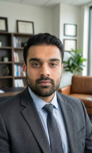Professional man in a suit, seated in an office setting with bookshelves and greenery, representing qualified educators at Chroma Early Learning Academy.
