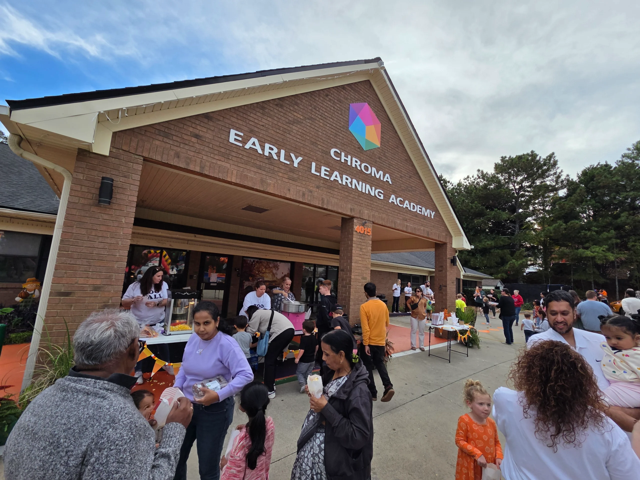 Chroma Early Learning Academy building with families enjoying an outdoor event, featuring staff serving food and children engaging in activities, emphasizing community involvement and early childhood education.