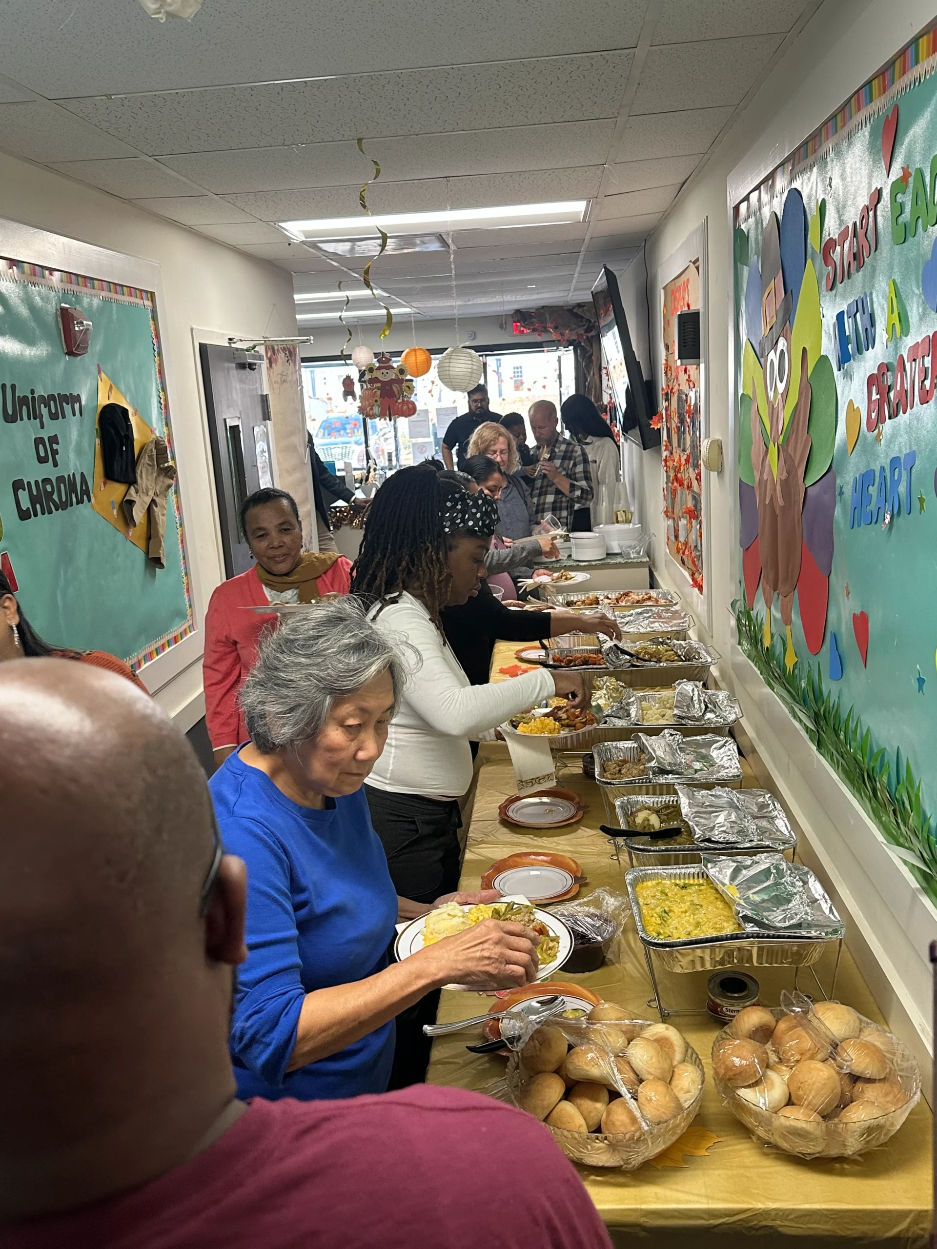 Community gathering at Chroma Early Learning Academy featuring families enjoying a buffet of diverse foods during a festive event, with decorations and a warm atmosphere.