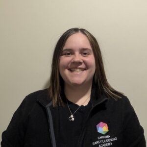 Nadine Wainehouse, Directora Ejecutiva de Chroma Early Learning Academy, sonriendo y vestida con chaqueta con el logotipo de la academia, fondo neutro.