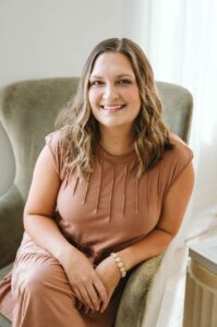 Mujer sonriendo sentada en un sillón, con cabello ondulado y vestimenta marrón, representando un ambiente acogedor y profesional, alineada con el enfoque de Chroma Early Learning Academy en la educación y el apoyo a las familias.